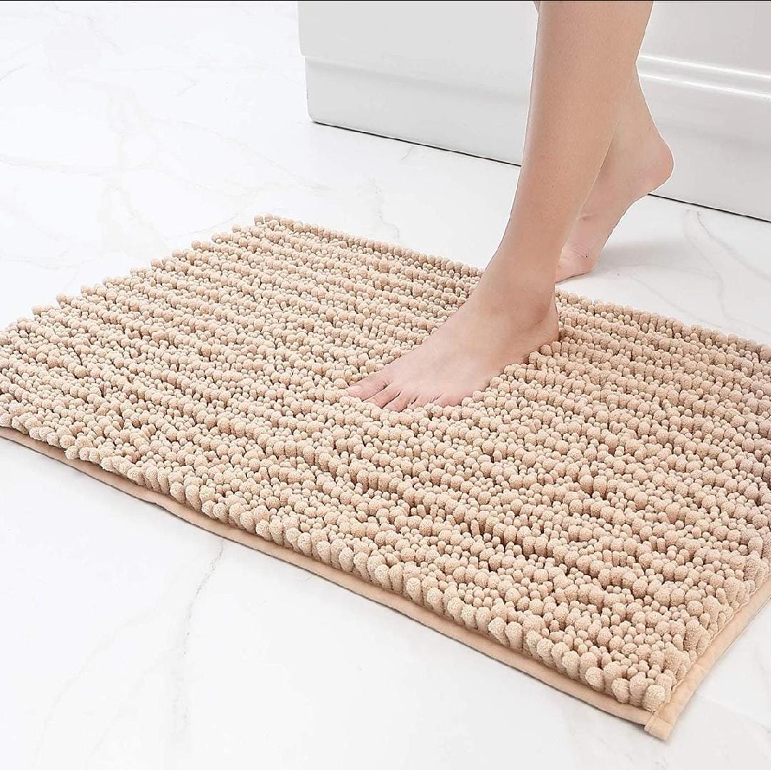 Beige bath mat on a white floor with a foot stepping onto it.