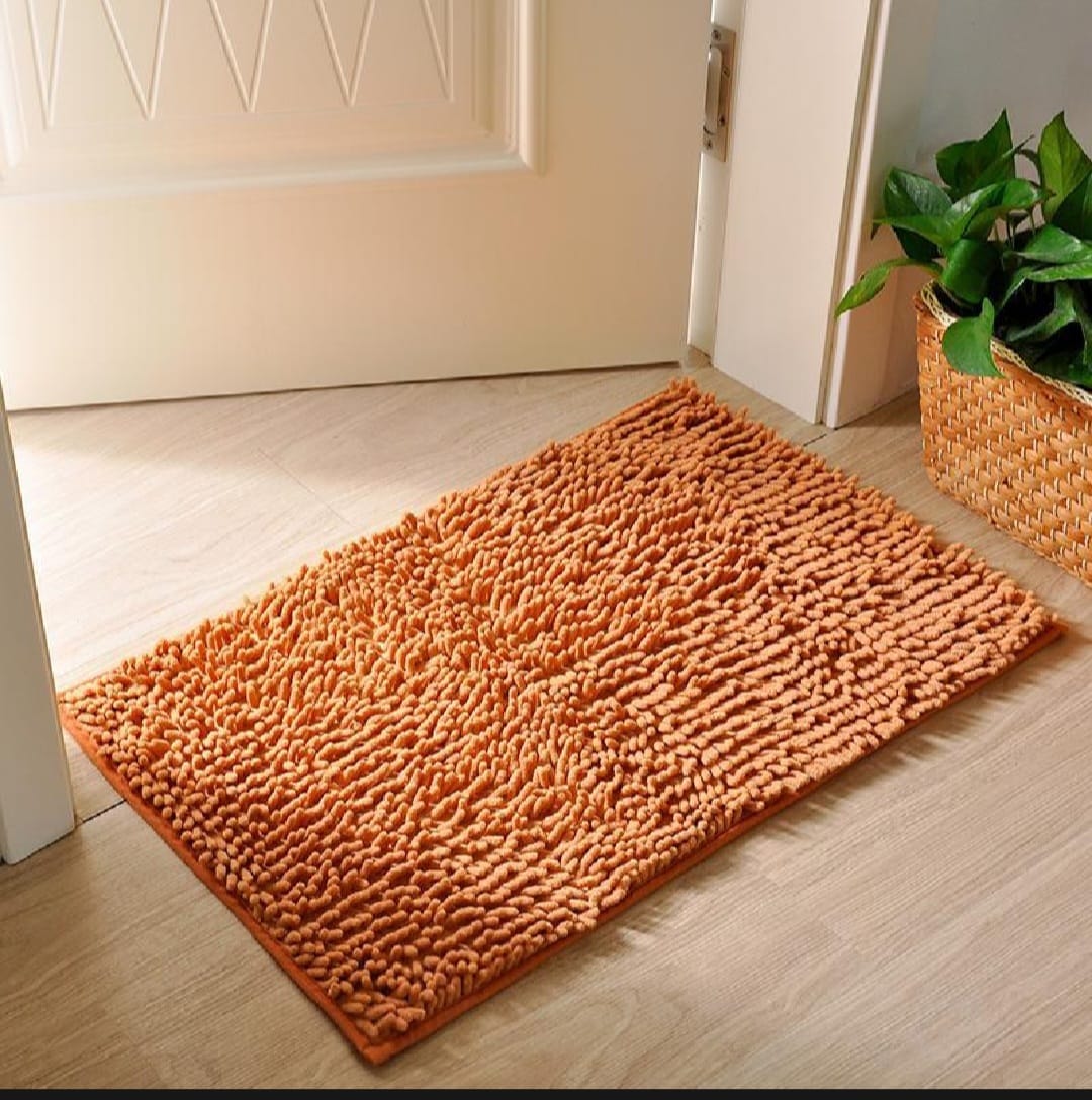 Orange doormat on a wooden floor with a plant in the background