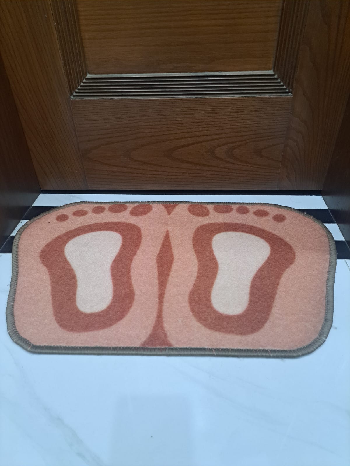 Doormat with footprints design on a white floor in front of a wooden door.