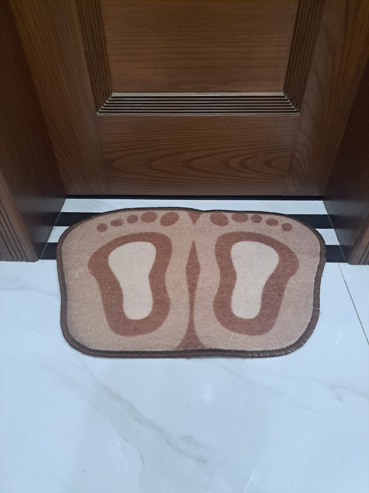 Doormat with footprints on a tiled floor in front of a wooden door.