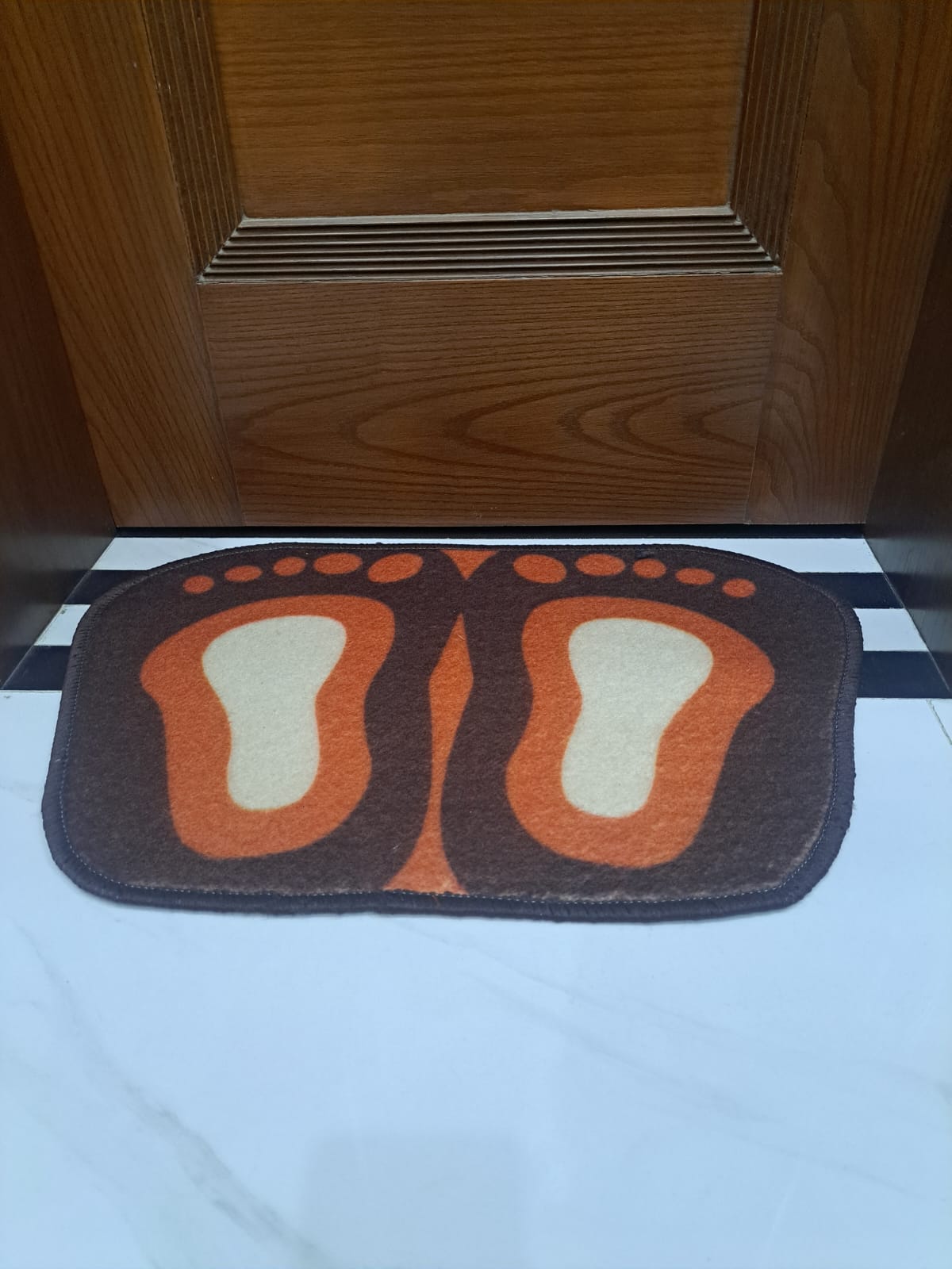 Doormat with footprints design on a floor in front of a wooden door.