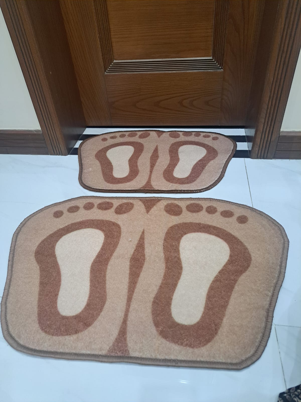 Two foot-shaped mats on a tiled floor in front of a wooden door.