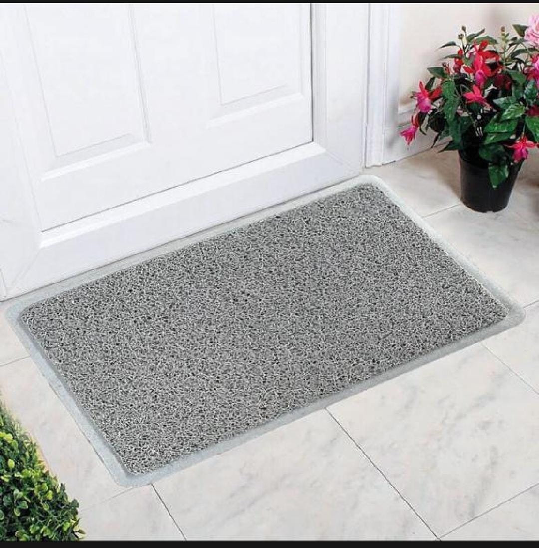 Gray doormat on a tiled floor with a white door and potted plant in the background