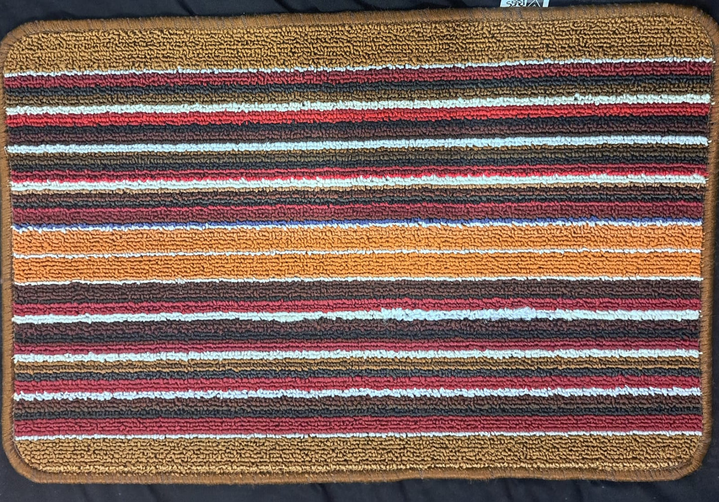 Multicolored striped doormat with a brown border on a dark background