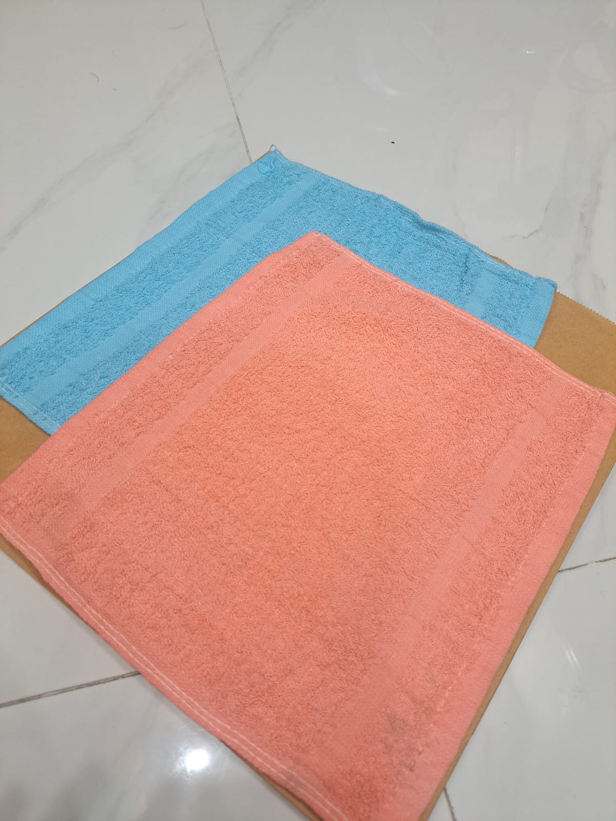Two towels, one blue and one pink, on a tiled floor.
