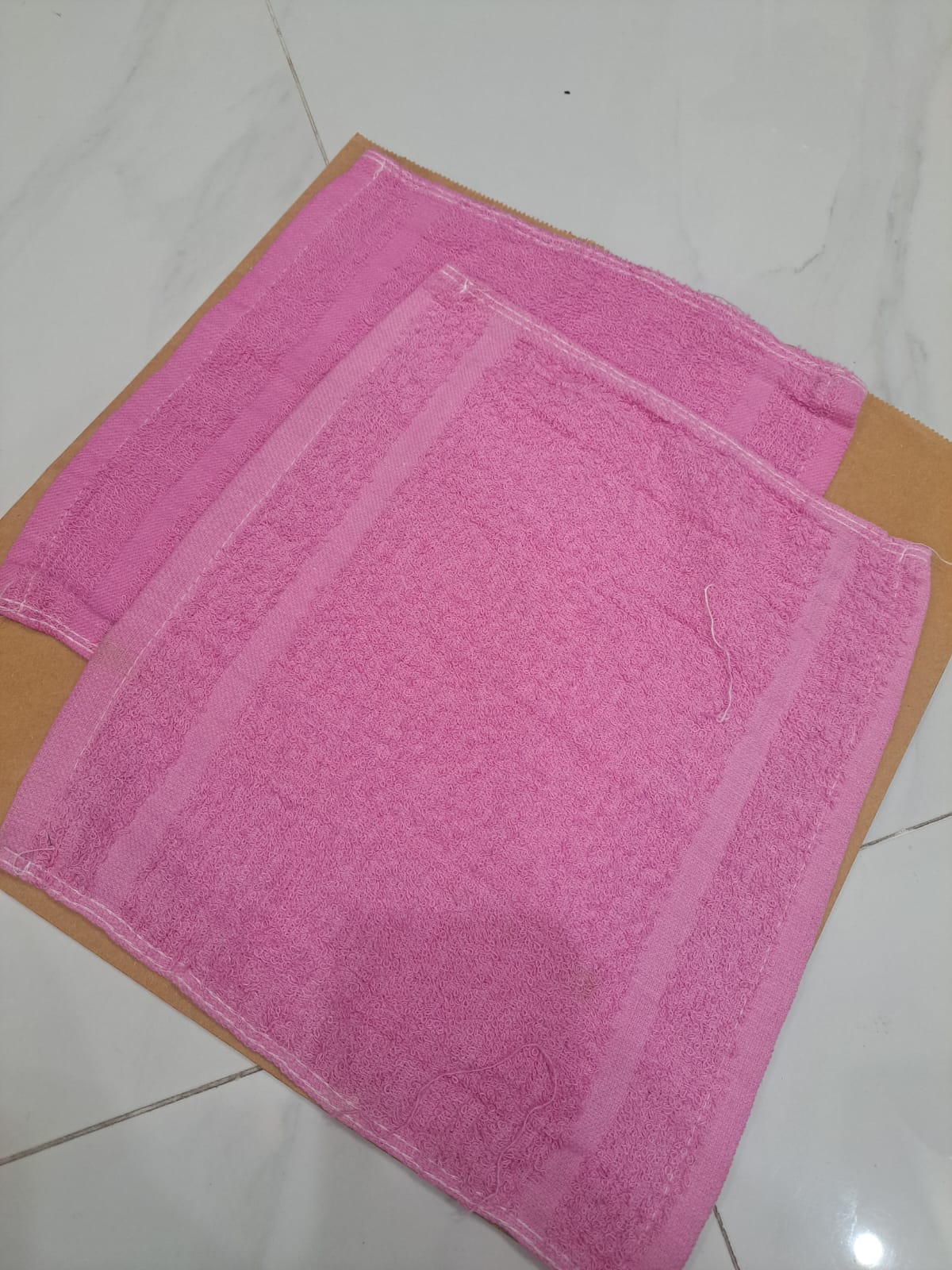 Two pink towels on a wooden surface with a white tiled floor background