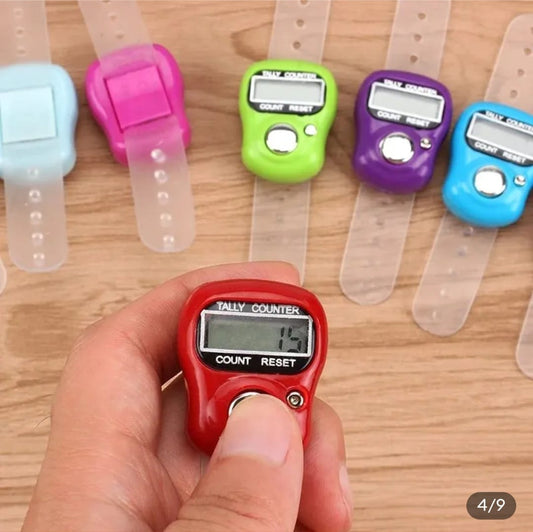 Hand holding a red digital finger counter with colorful clip-on counters in the background.