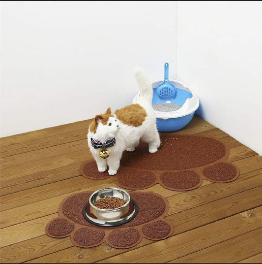 Two small dogs standing on a paw-shaped mat with a bowl of food in front of them, next to a blue litter box.