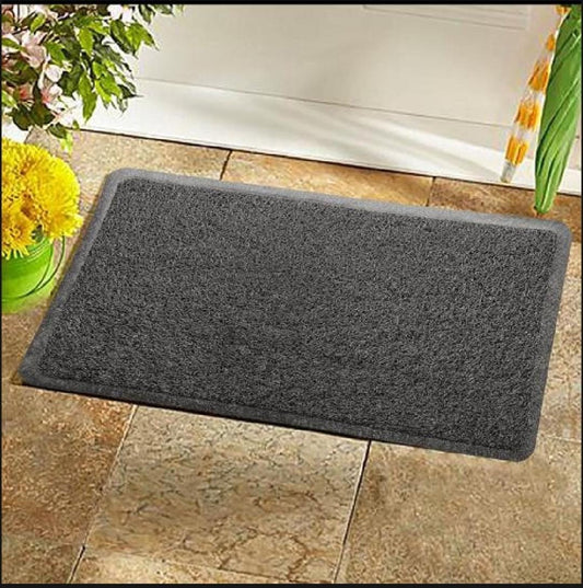 Gray doormat on a stone floor with flowers and a white door in the background