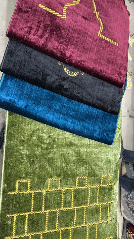 Three textured prayer mats in red, black, and blue on a green fabric background.